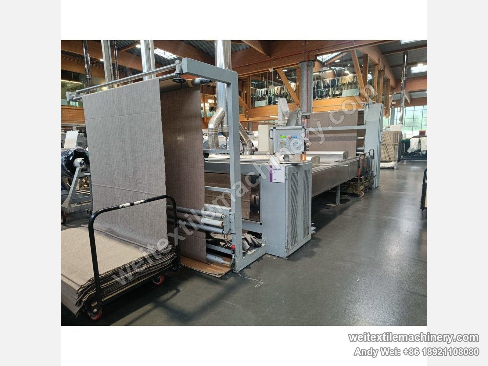 Used CoMaR VAPORAMA belt-type steaming-shrinking machine, entry end, fabric fed from a trolley over the overhead frame, panel and steam boxes along the machine