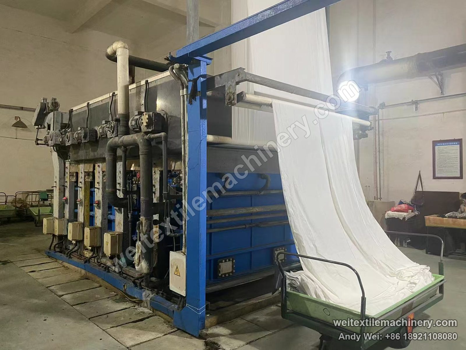 Used Kroy Fabric Machine wool fabric chlorination line, three-quarter view with a row of geared motors, valve boxes, blue tanks and fabric into the trolley