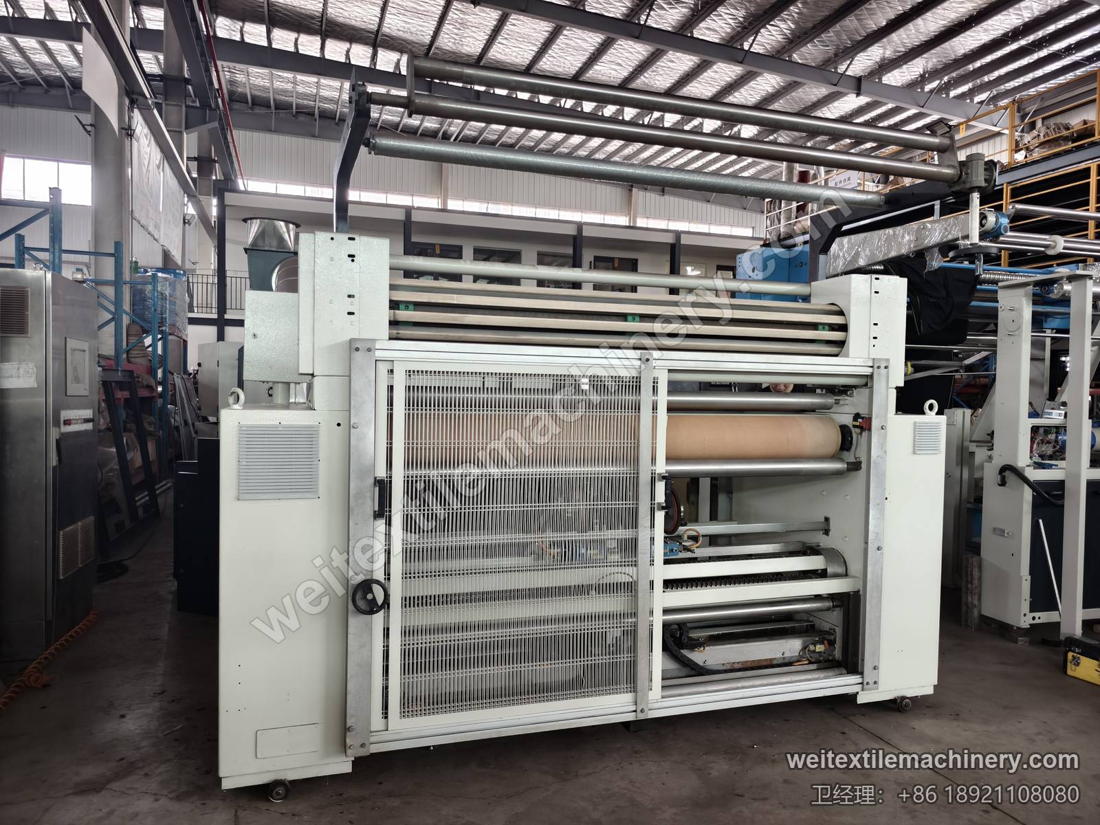 二手 Bianco Tramatex SP04 针轮式整纬机正面，网格护门、顶部导布辊组与包膜辊筒