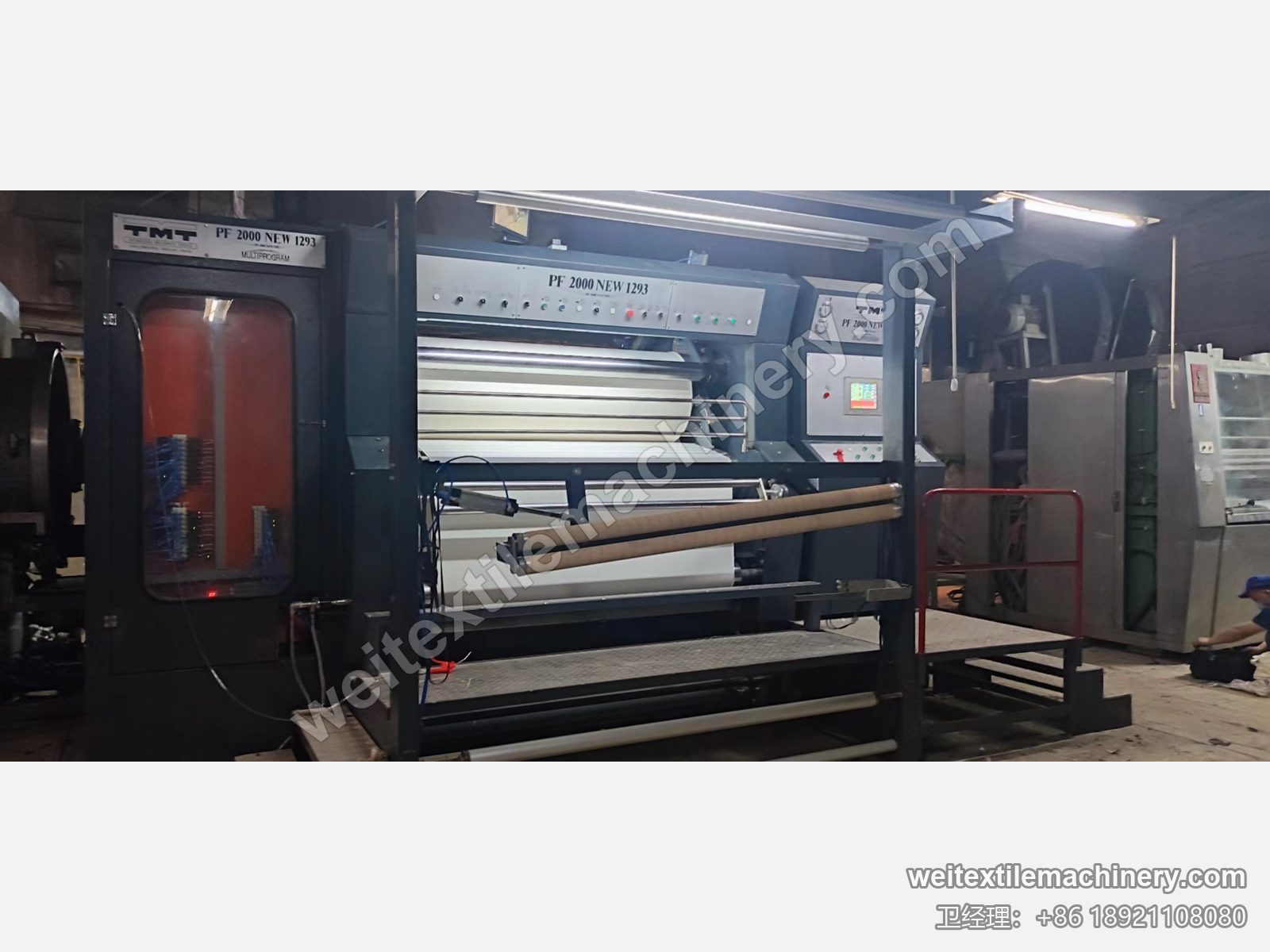 二手 TMT PF 2000 NEW 1293 罐蒸机，机身 PF 2000 NEW 1293 标识、卷布辊上的织物与红色护栏