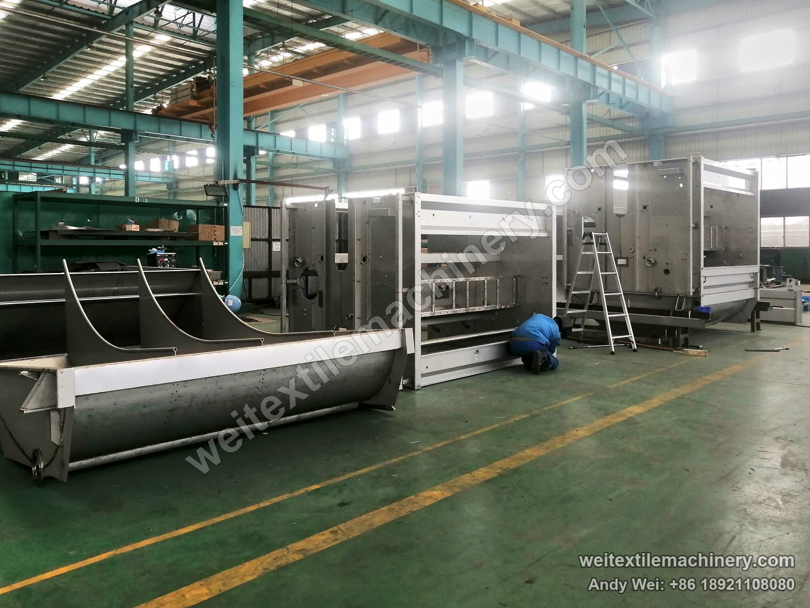 WPF-4XS four-channel wool scouring and milling machine in build: stainless steel frames standing, half-round tanks on the floor, one operator at work