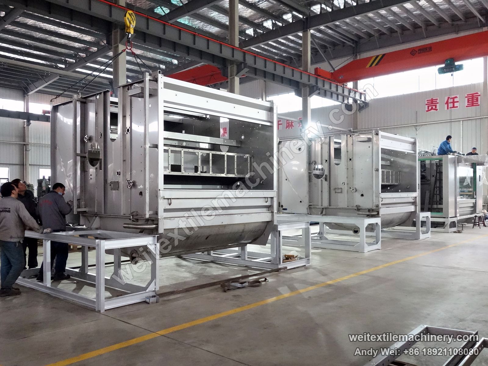 WPF-4XS in build: several machine bodies in a row on stands, operators alongside, red overhead crane above
