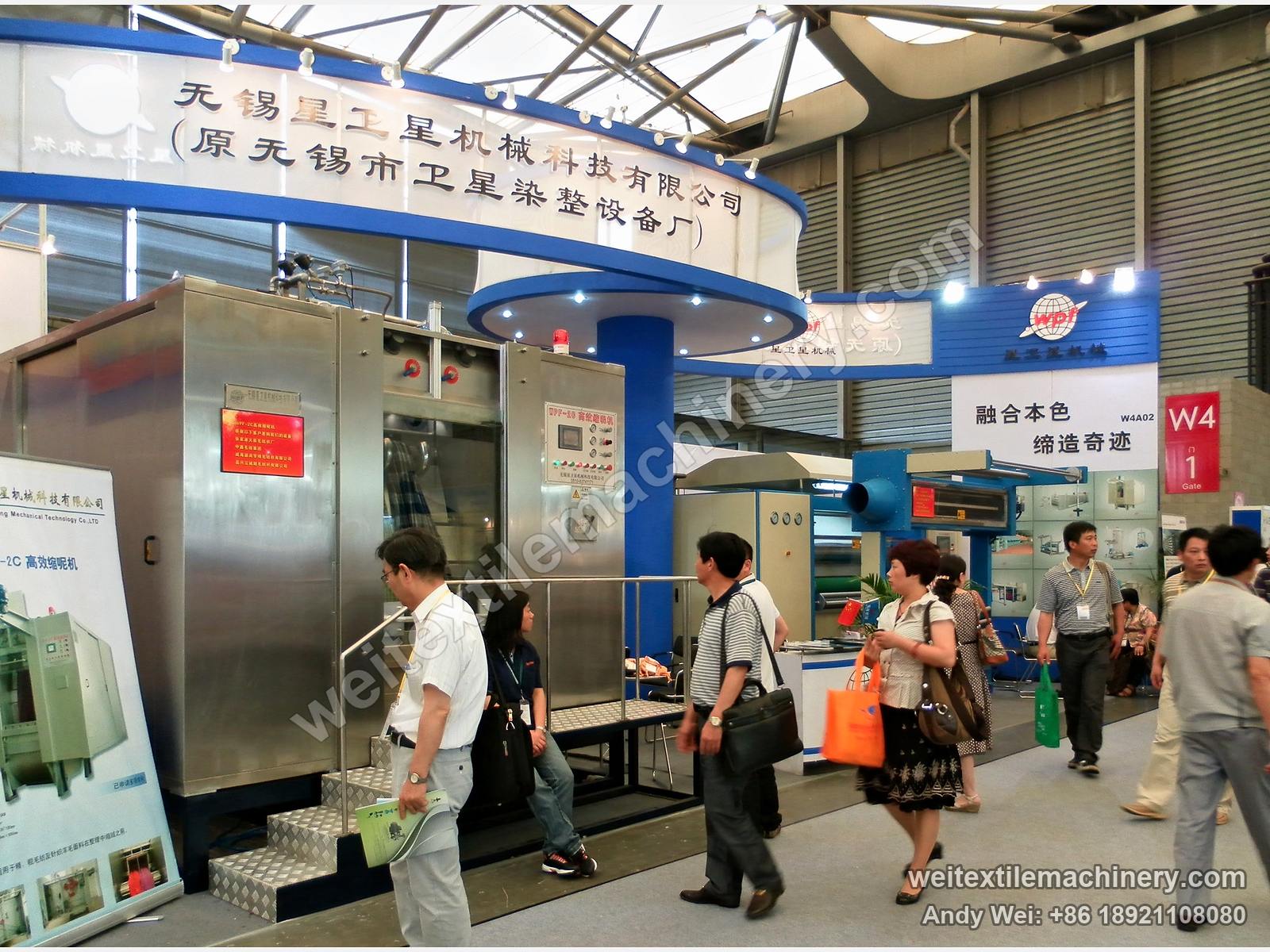 The 2010 stand of Xingweixing Machinery, the earlier name of QL, under a fascia reading Wuxi Xingweixing Machinery Technology (formerly Wuxi Weixing Dyeing & Finishing Equipment Works), with visitors passing