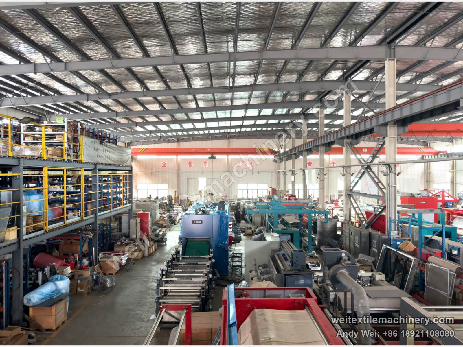 Elevated view of the QL workshop: two-level storage racks on the left, rows of machines in the bay and red overhead cranes