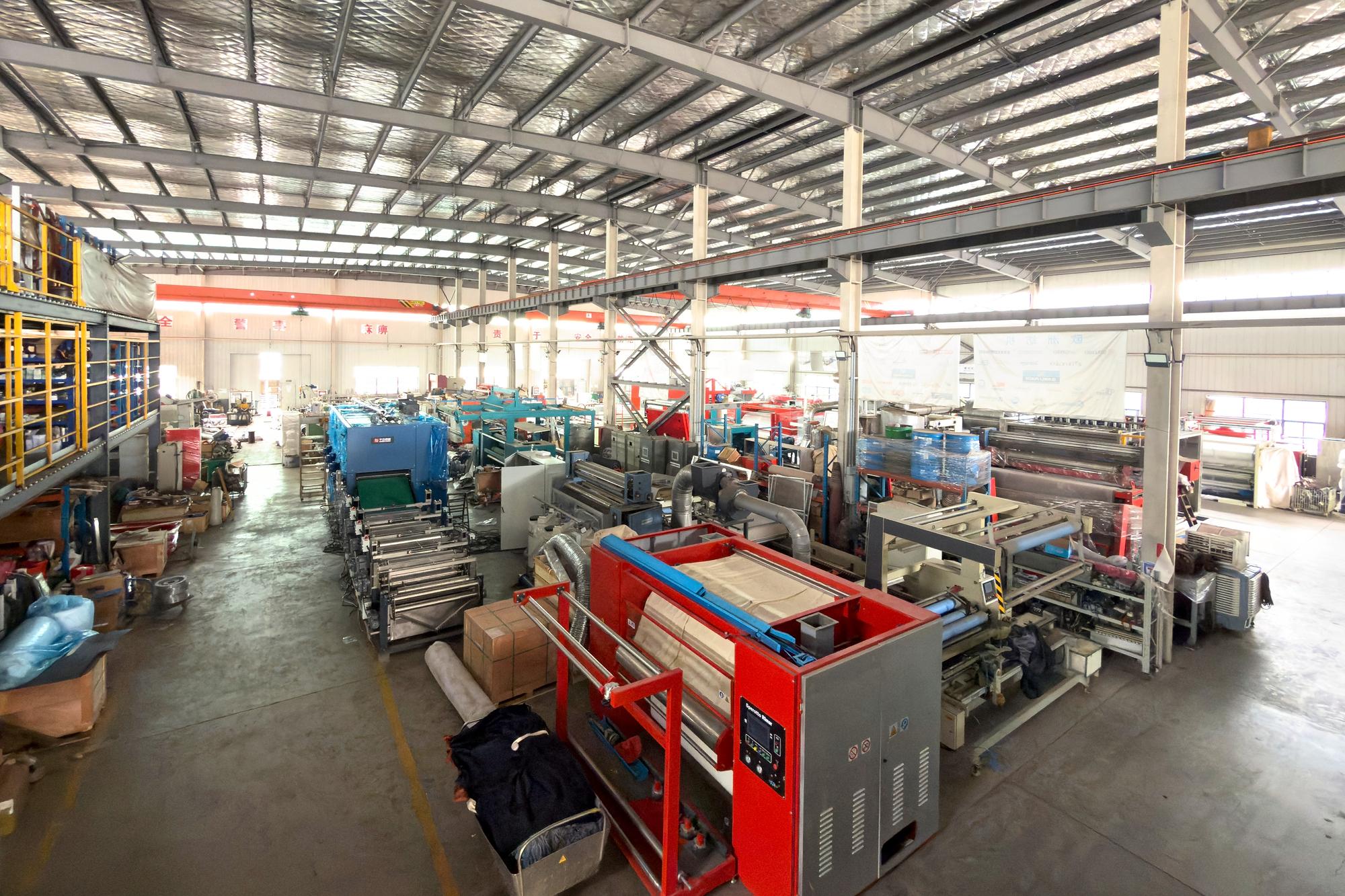 Inside the QL workshop: several machines under a steel-frame roof, a two-level storage rack on the left and a red machine in the foreground