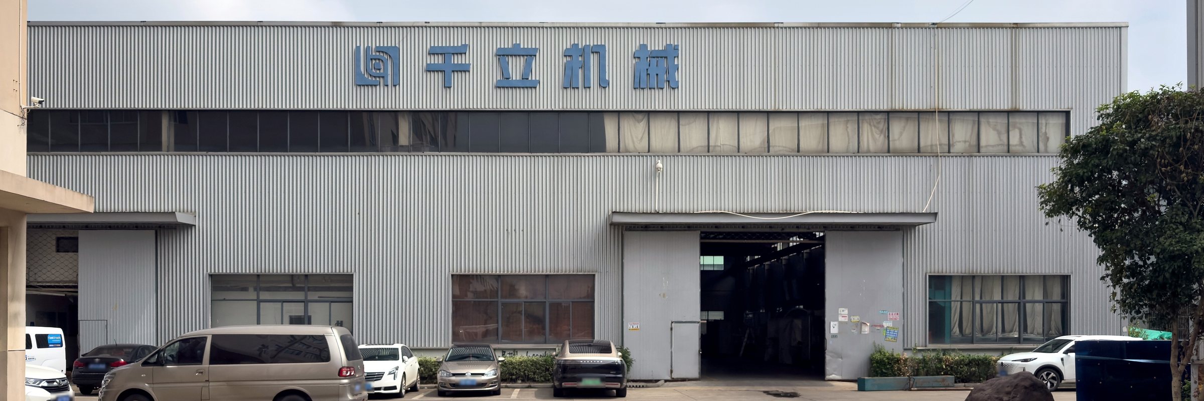 千立机械厂房外观，墙面有「千立机械」标识，门前为停车场
